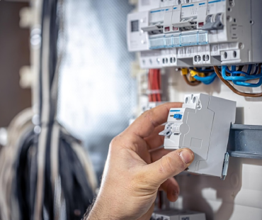 A person’s hand installs an electrical circuit breaker into a control panel with multiple wires and switches visible in the background, showcasing skills essential in general contracting.