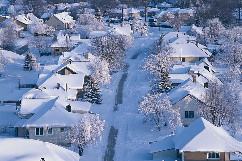 Aerial view of a residential neighborhood covered in snow; houses, trees, and streets are blanketed in white, highlighting rooftops—an ideal scene to showcase expert roofing and general contracting services for winter maintenance.